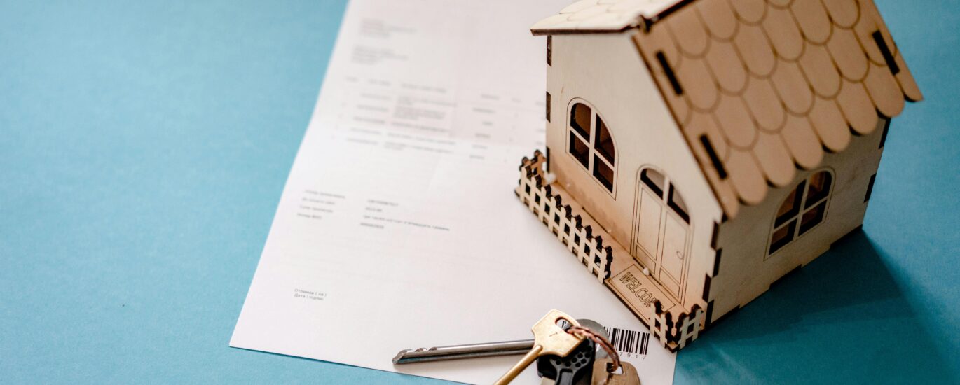Miniature wooden house with keys and contract symbolizing real estate transactions.