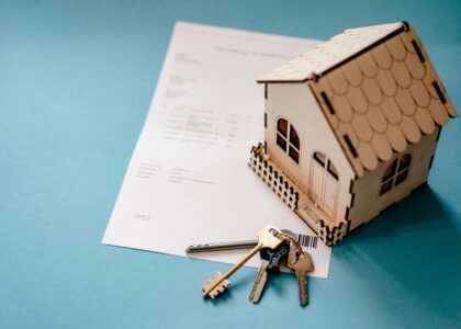 Miniature wooden house with keys and contract symbolizing real estate transactions.