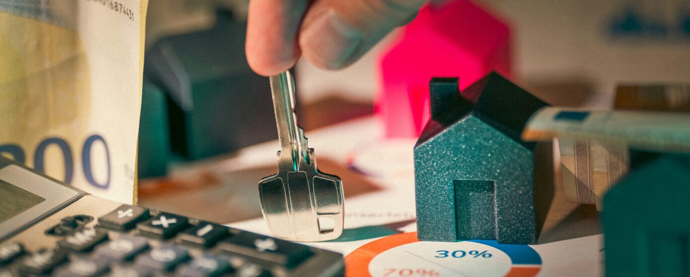 A close-up of real estate financial planning with keys, calculator, and money.