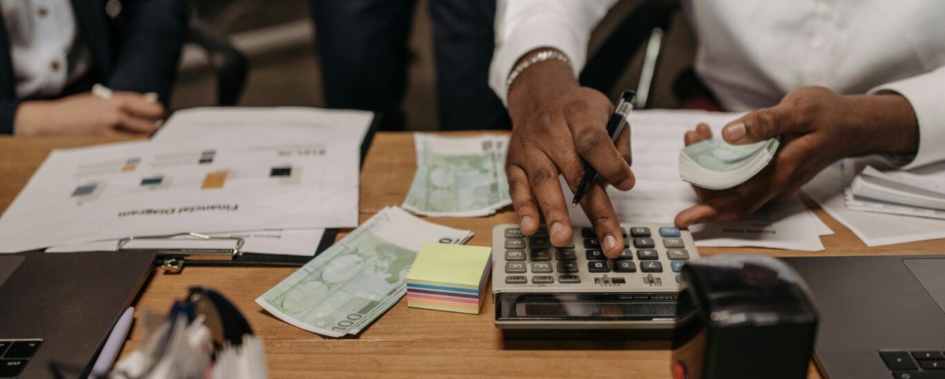 Professional setting with people handling cash and calculations using a calculator at a desk.