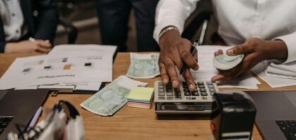 Professional setting with people handling cash and calculations using a calculator at a desk.