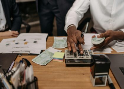 Professional setting with people handling cash and calculations using a calculator at a desk.